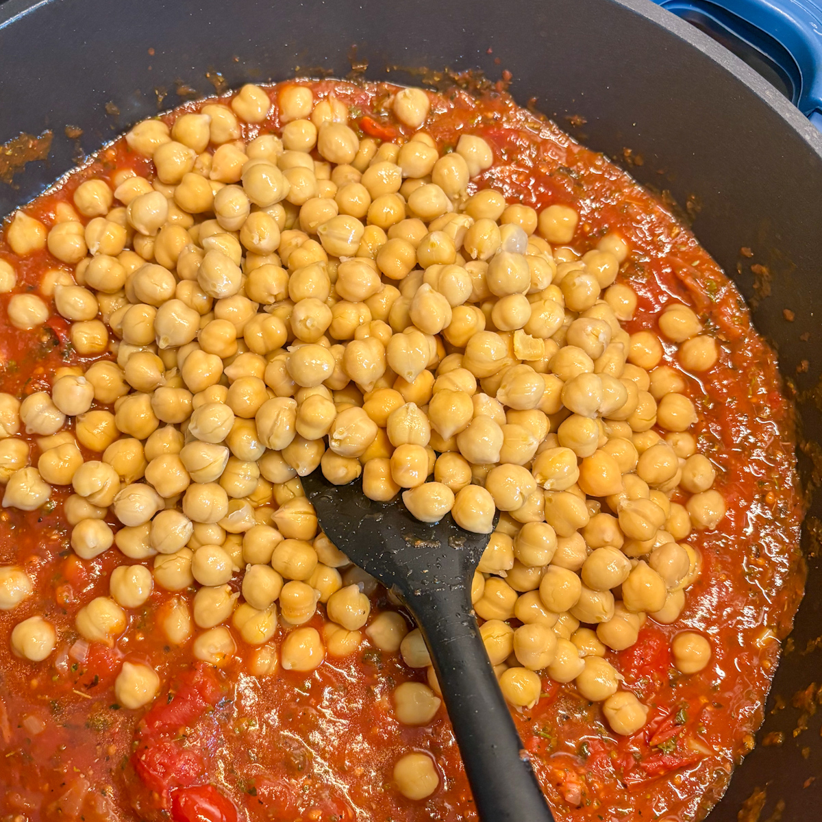 Rinsed chickpeas added to rich tomato sauce in a pan for chickpeas in tomato sauce