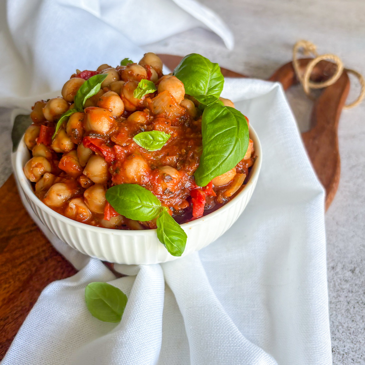  Bowl of chickpeas in tomato sauce garnished with whole basil leaves