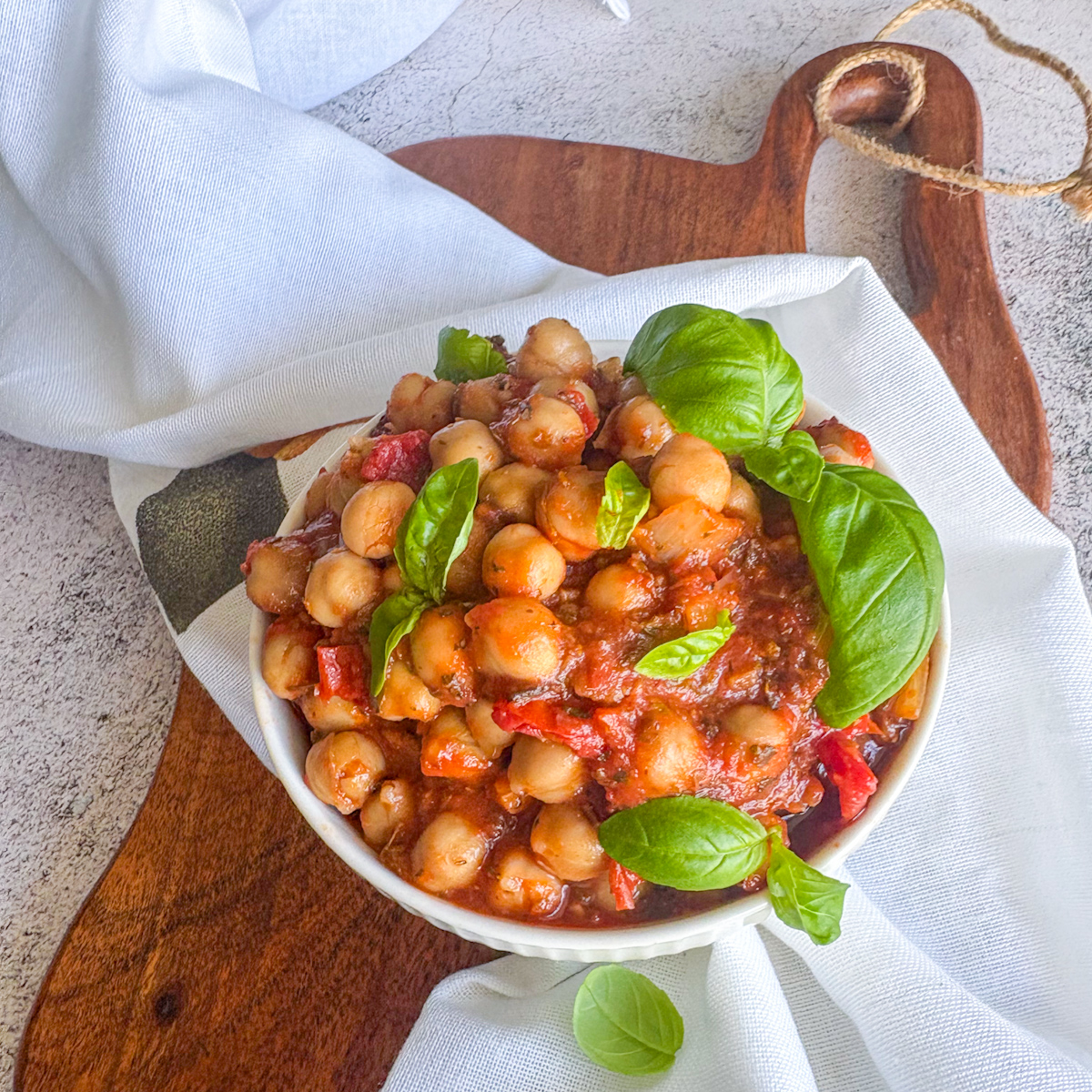 Saucy chickpeas in tomato sauce in a white bowl, finished with fresh basil