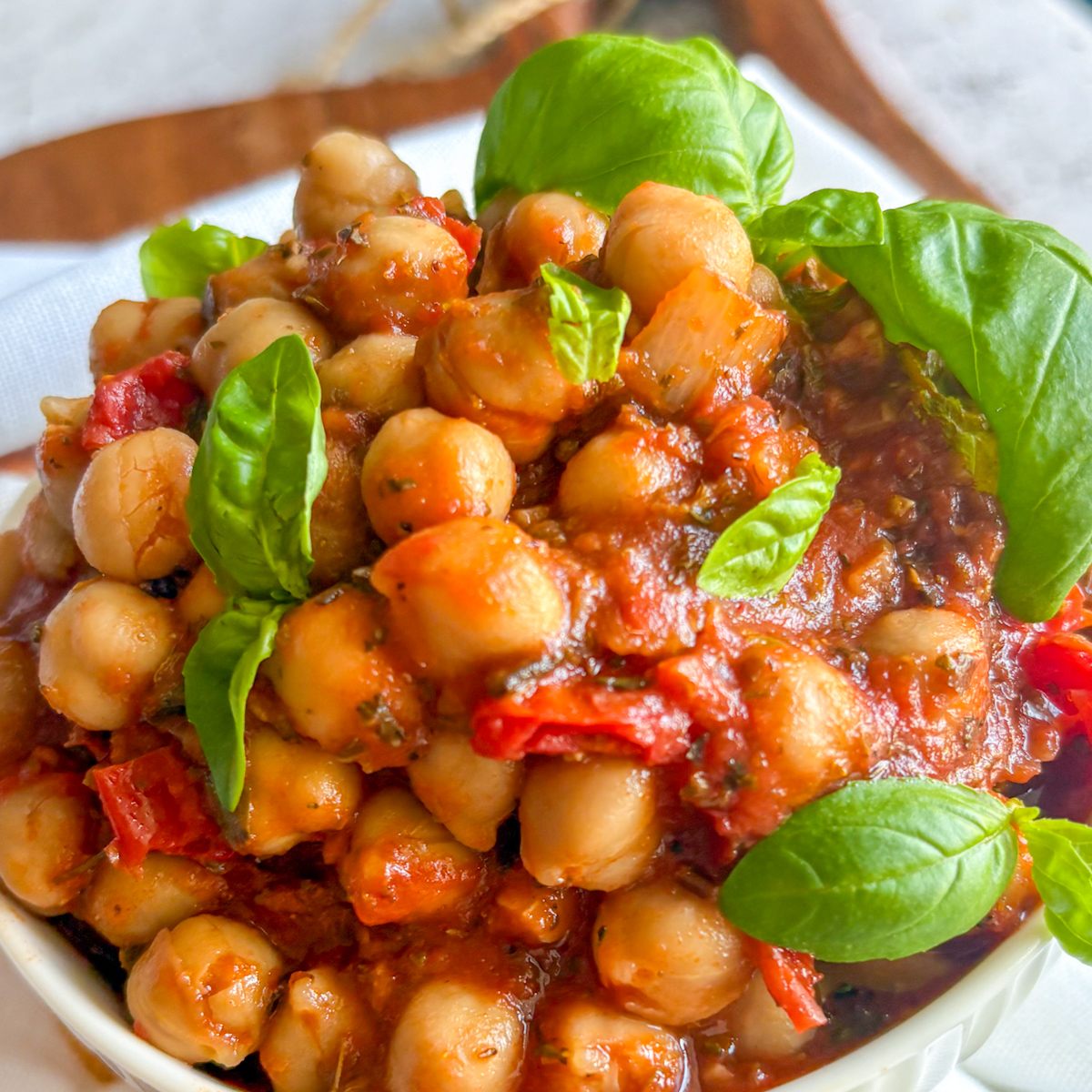 Budget-friendly chickpeas in tomato sauce in a fluted white bowl with fresh basil