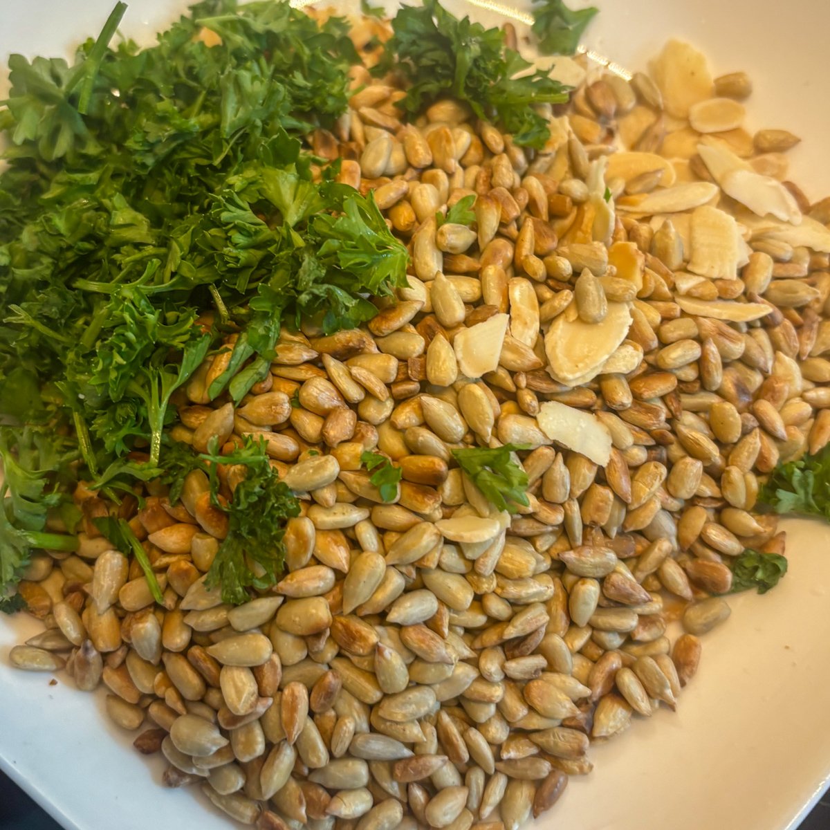 Crunchy chilled carrot soup topping of toasted sunflower seeds, almond flakes and fresh curly parsley on a plate.