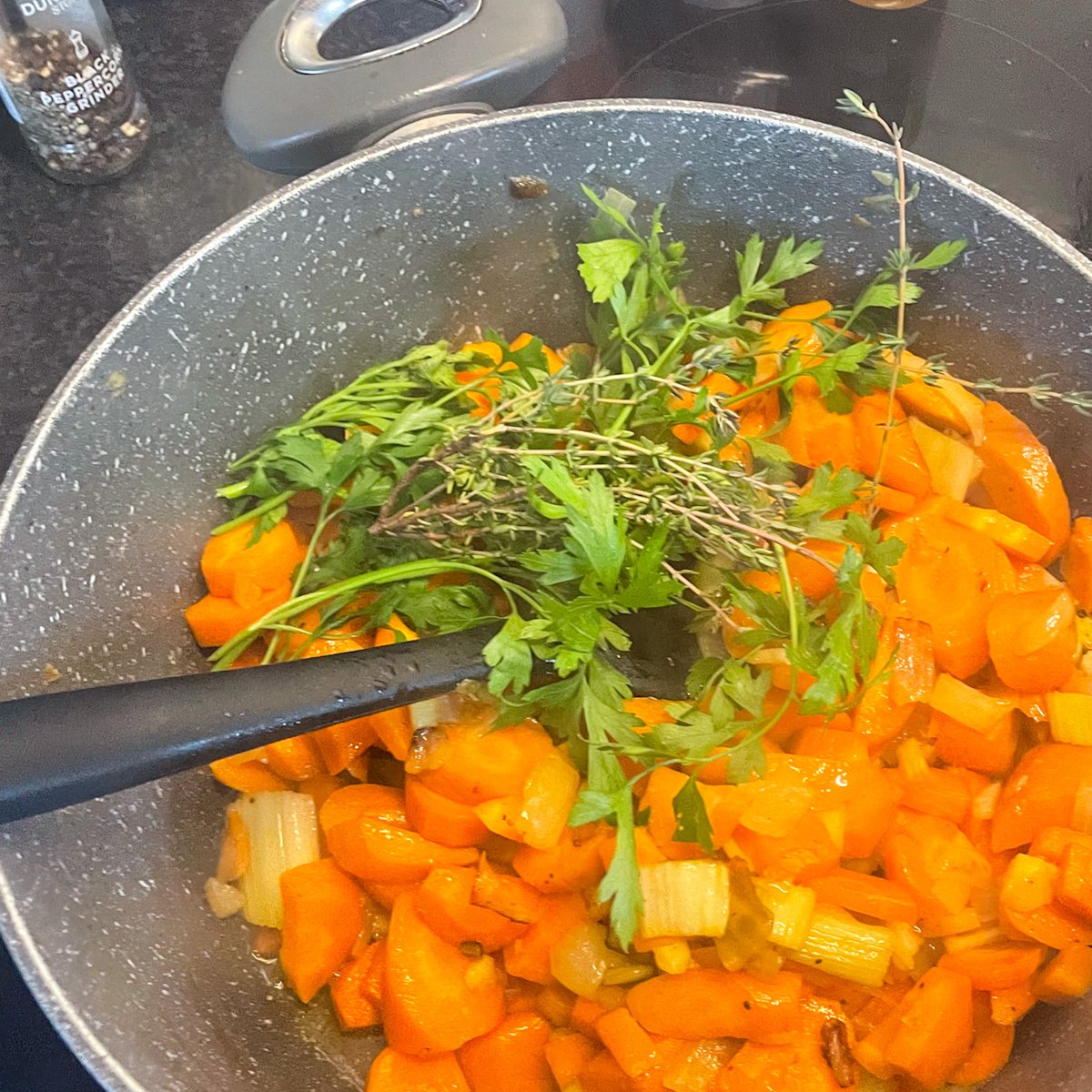  Golden sautéed carrots, onion and celery in a pan with thyme and parsley sprigs for chilled carrot soup base.