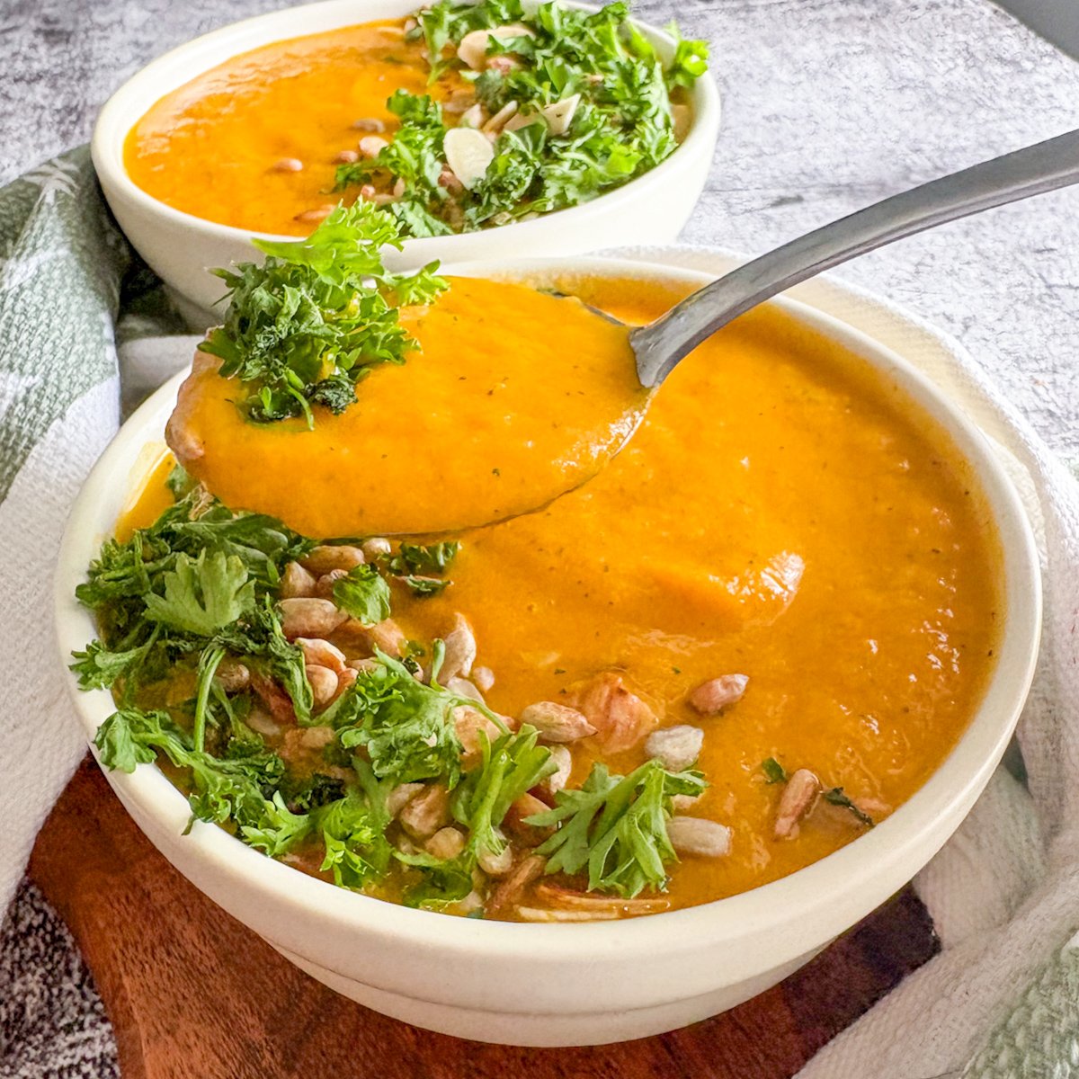 Velvety chilled carrot soup with a spoon scooping a portion, garnished with parsley and toasted seeds.