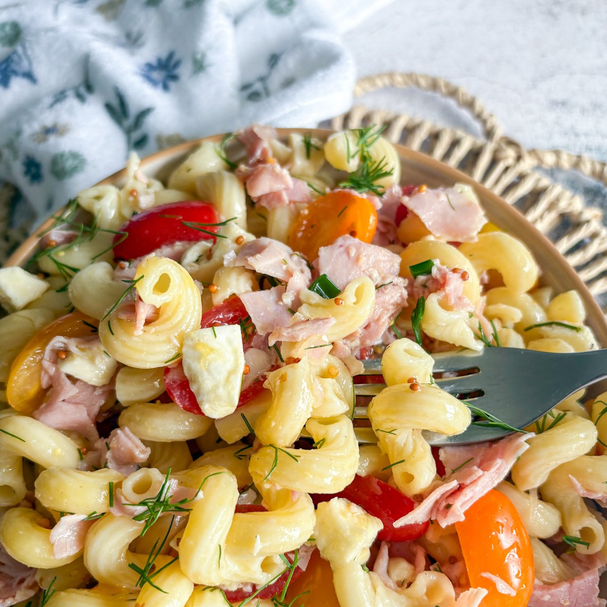 Pasta salad with dill vinaigrette, fork lifting macaroni beside orange cherry tomatoes