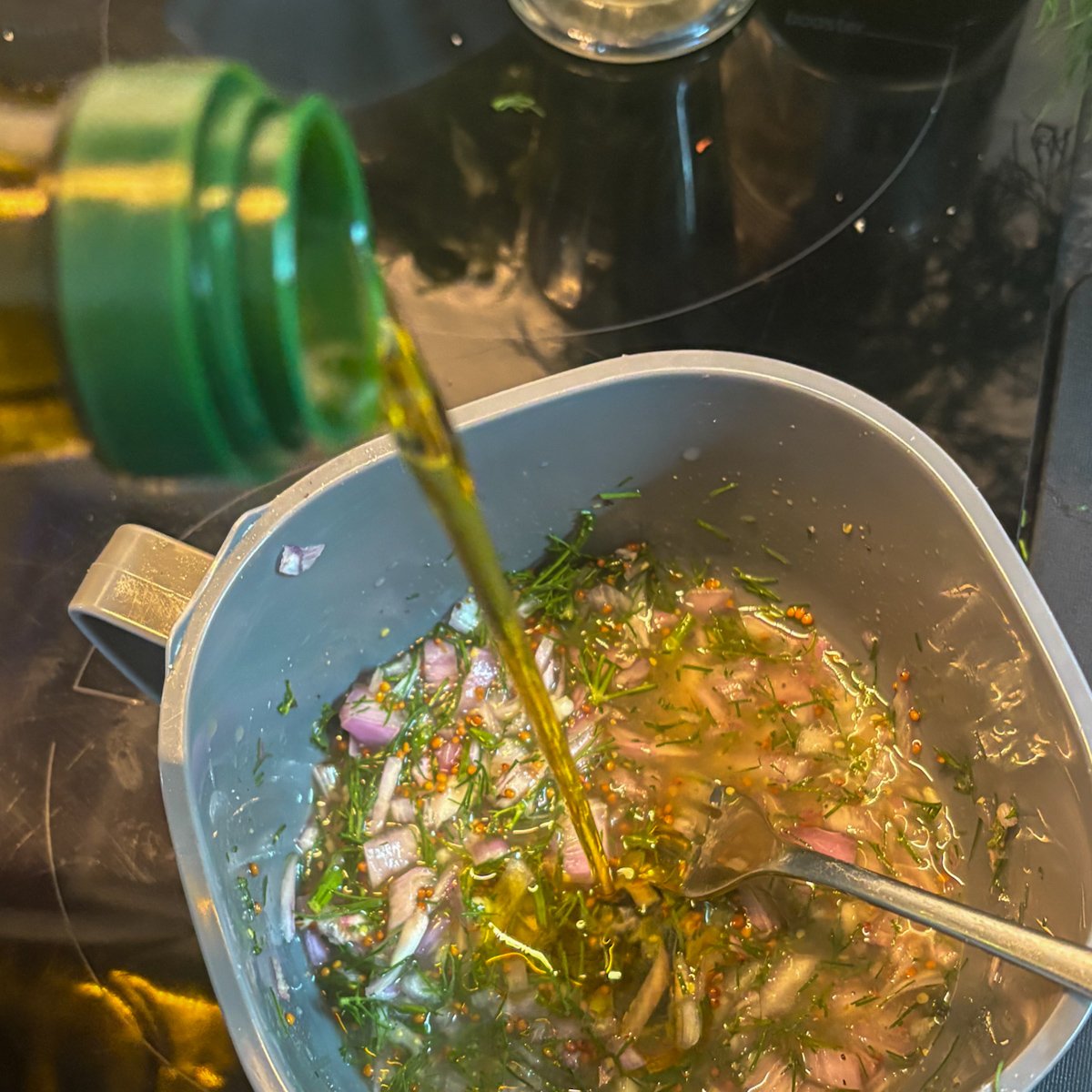 Whisking olive oil into dill vinaigrette for pasta salad, oil pouring into bowl