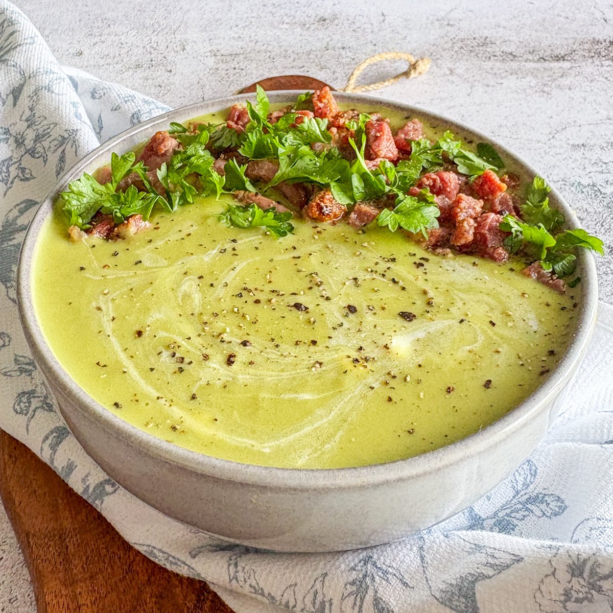 Silky pea soup with bacon and parsley garnish in a rustic grey bowl
