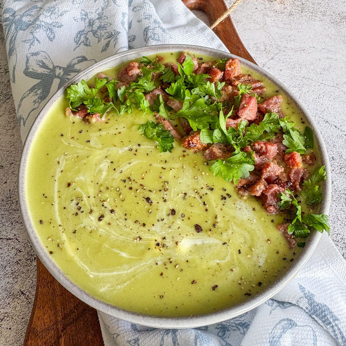 Creamy pea soup with bacon and parsley served on a blue floral napkin