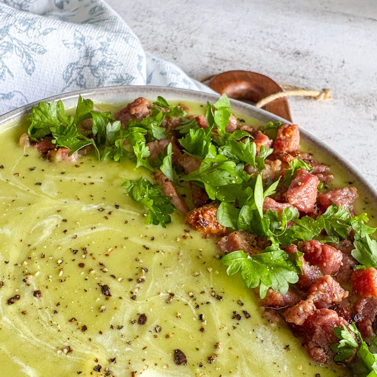 Close-up of creamy pea and bacon soup topped with bacon and fresh parsley