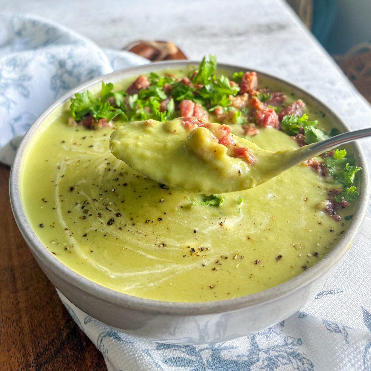 Creamy pea soup with bacon and parsley, spoon lifting a portion from the bowl