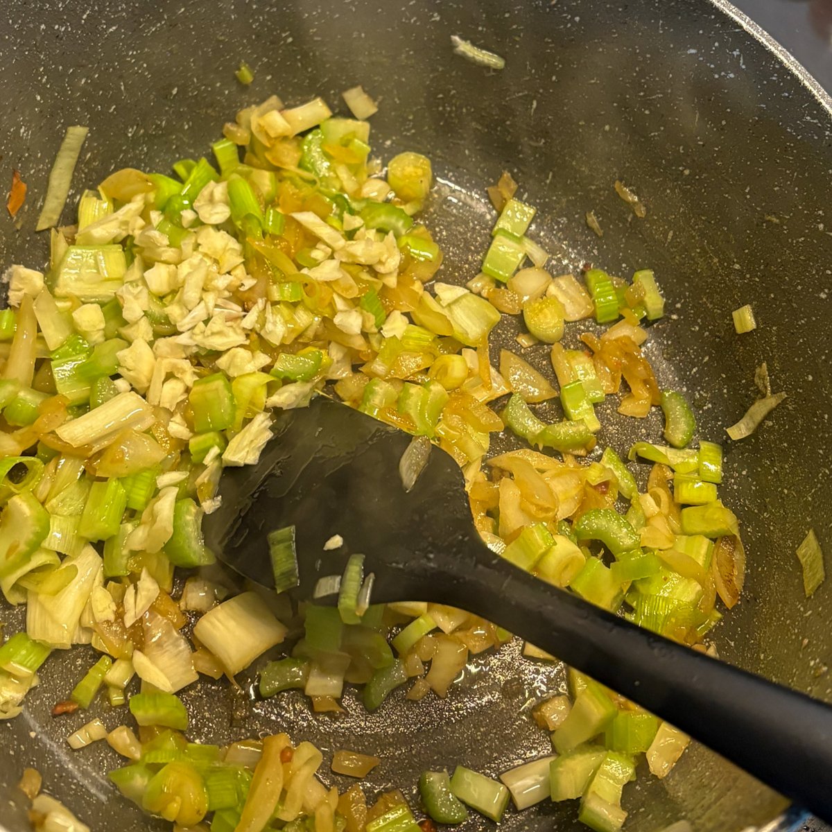 Leeks, celery and garlic softening in bacon fat for pea soup with bacon