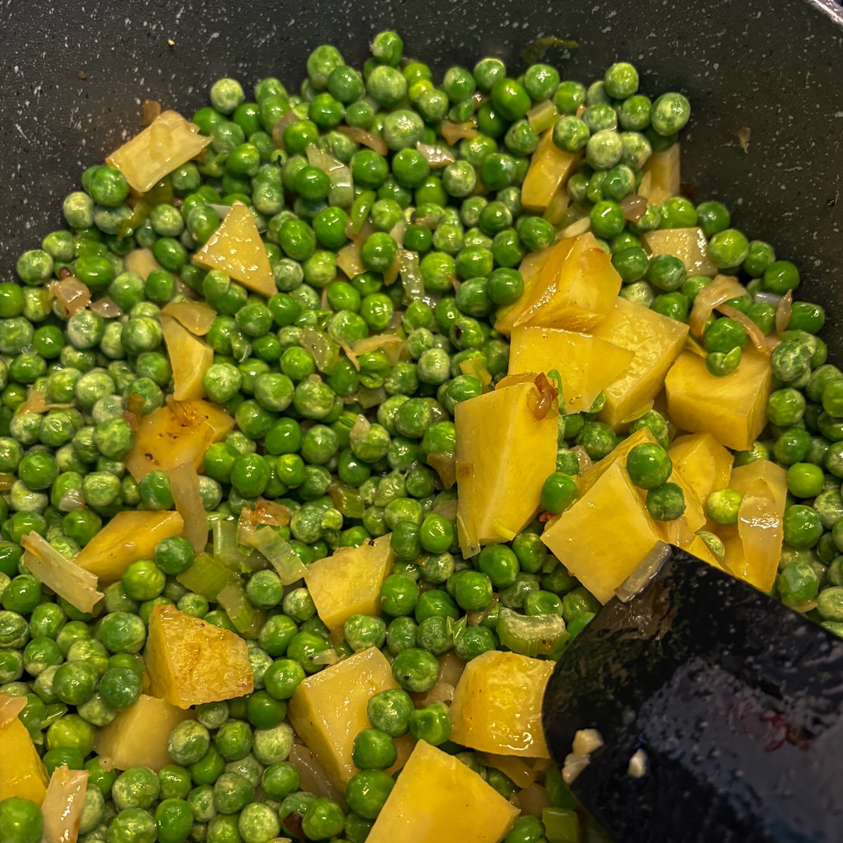 Peas and potato cubes coated in bacon fat in the pot for pea and bacon soup