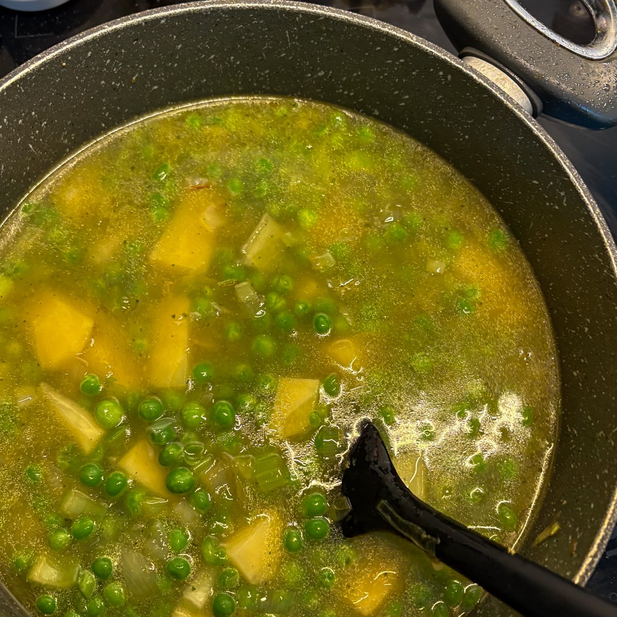 Pea soup with bacon before blending, peas and potato cubes simmering in stock