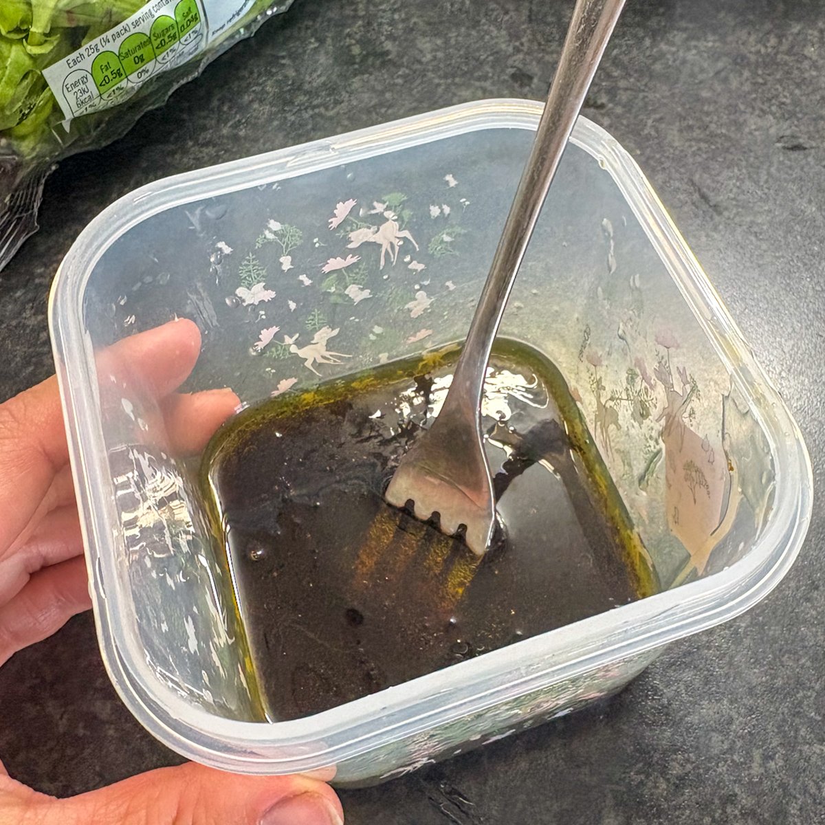 Honey balsamic dressing in a tub with a fork for peach and burrata salad