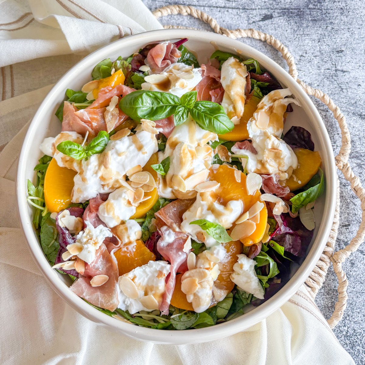 Close-up peach and burrata salad with basil sprig, almonds and balsamic drizzle