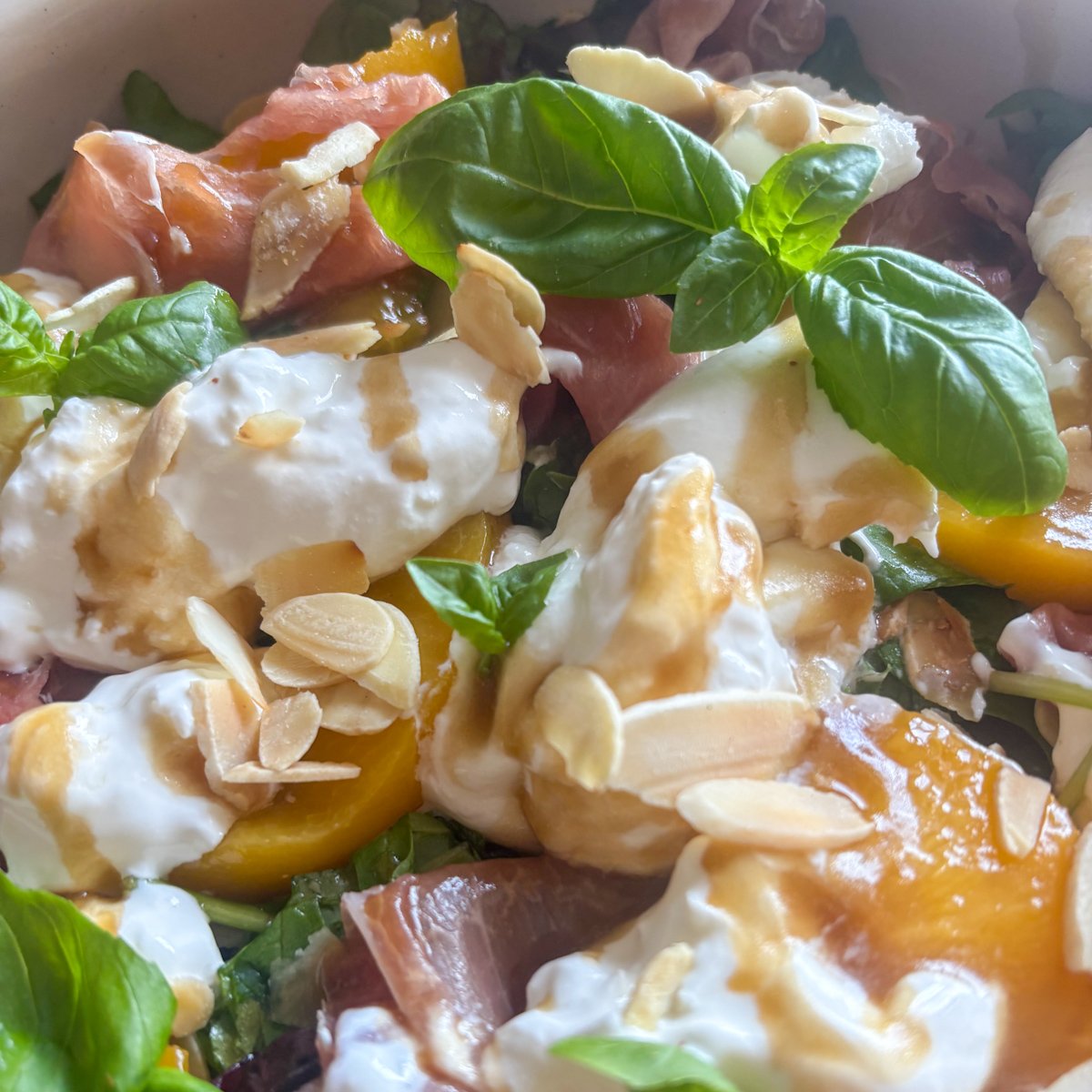 Peach and burrata salad base with peach slices, prosciutto and green leaves