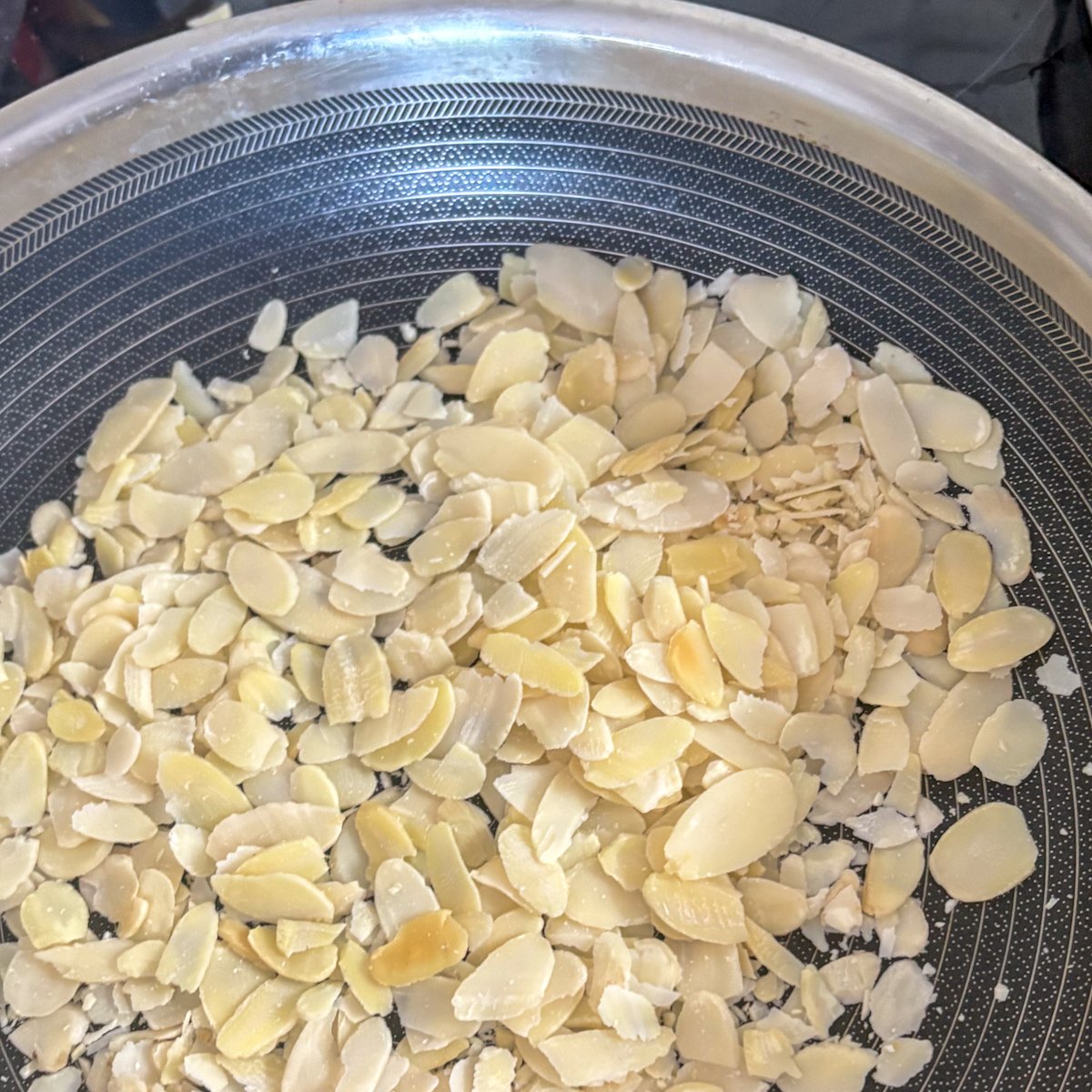 Flaked almonds toasting in a pan for peach and burrata salad
