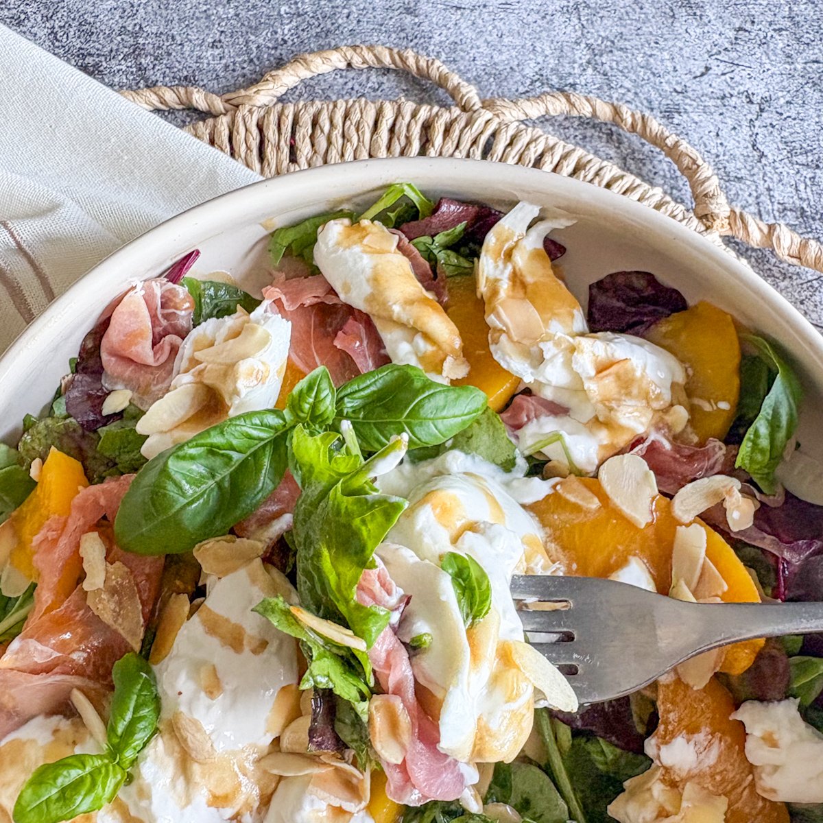  Fork lifting torn burrata and basil over peach and burrata salad with almonds
