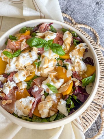 Peach and burrata salad in a bowl with prosciutto, basil and toasted almonds