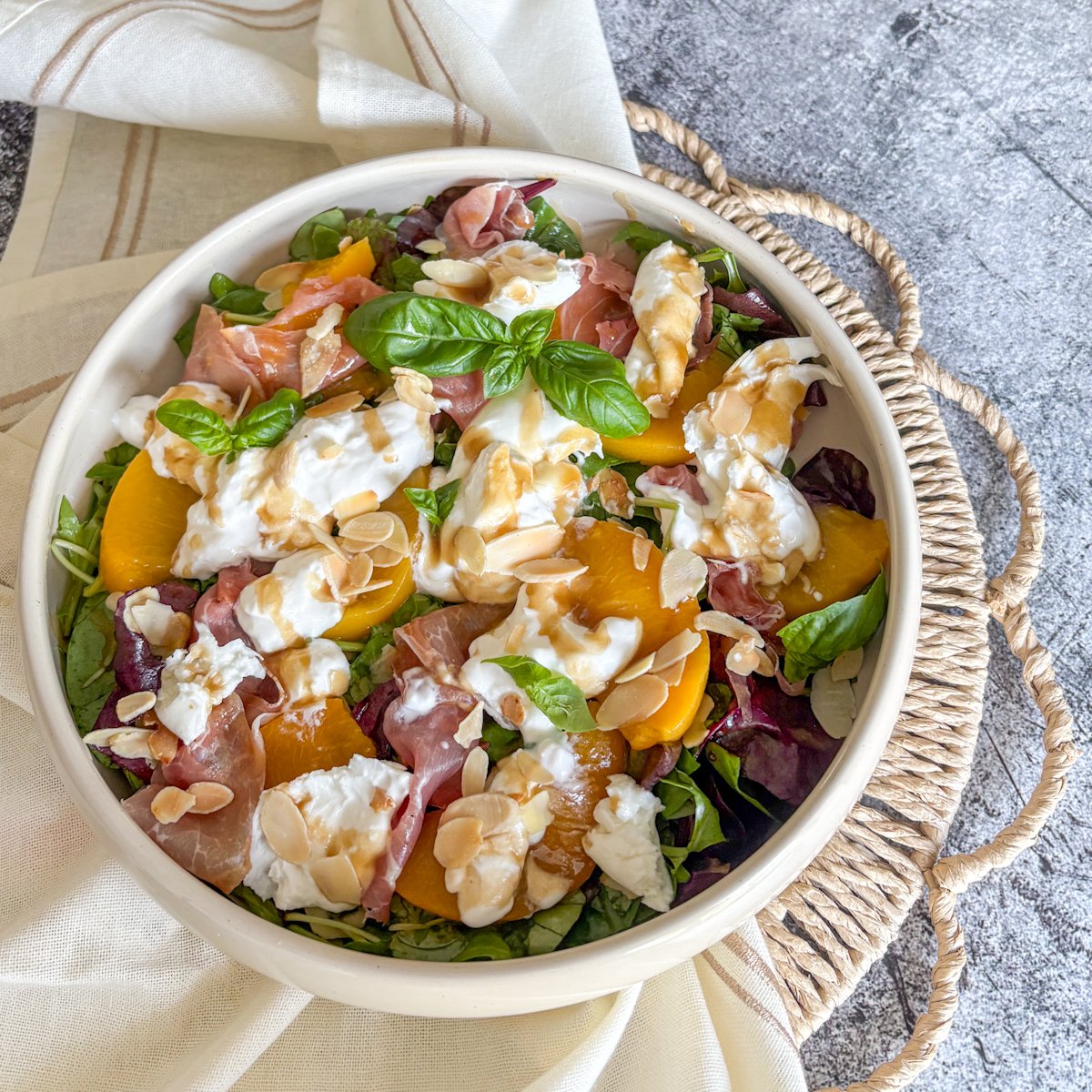 Peach and burrata salad in a bowl with prosciutto, basil and toasted almonds