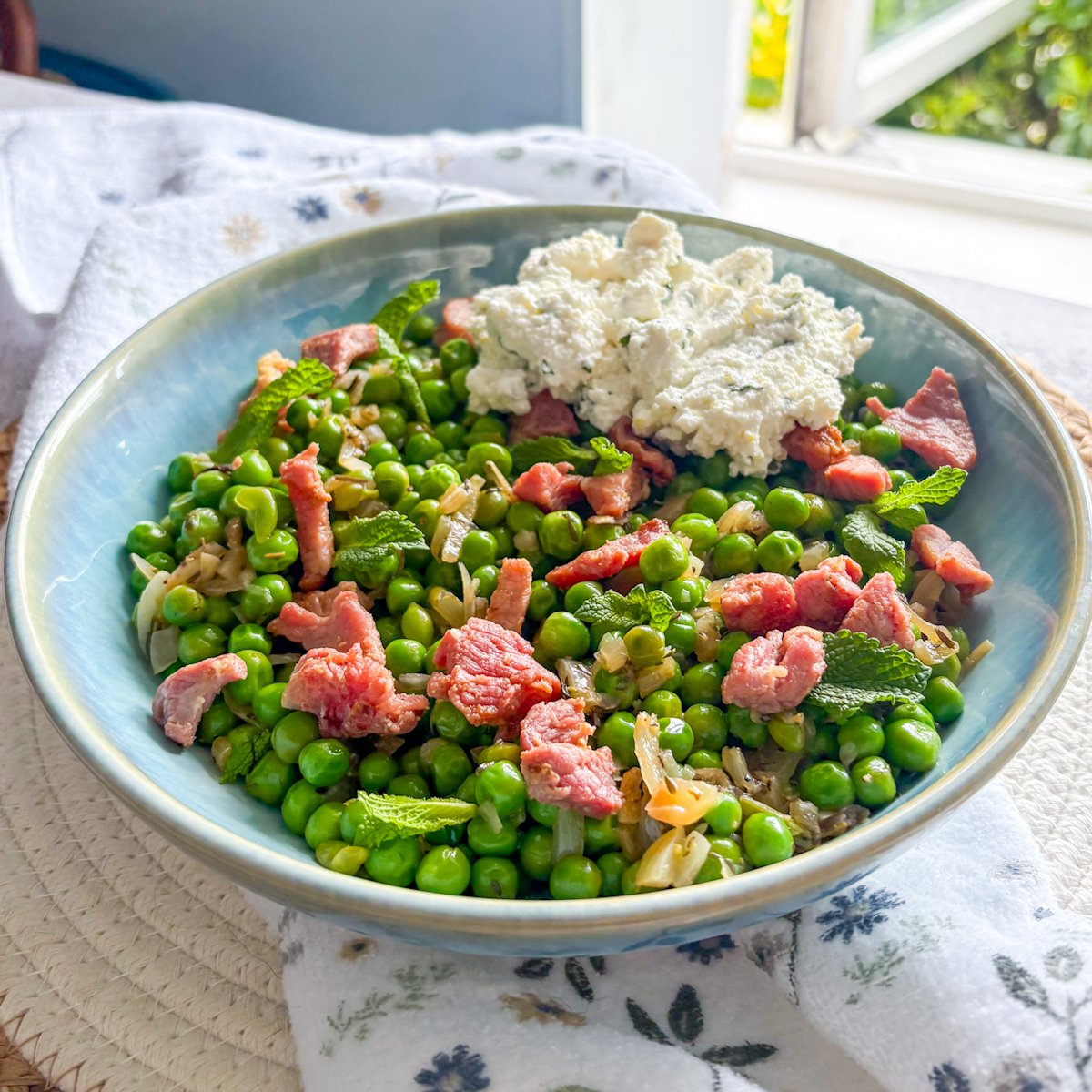 Sweet green peas with bacon and ricotta and torn mint in a rustic blue bowl