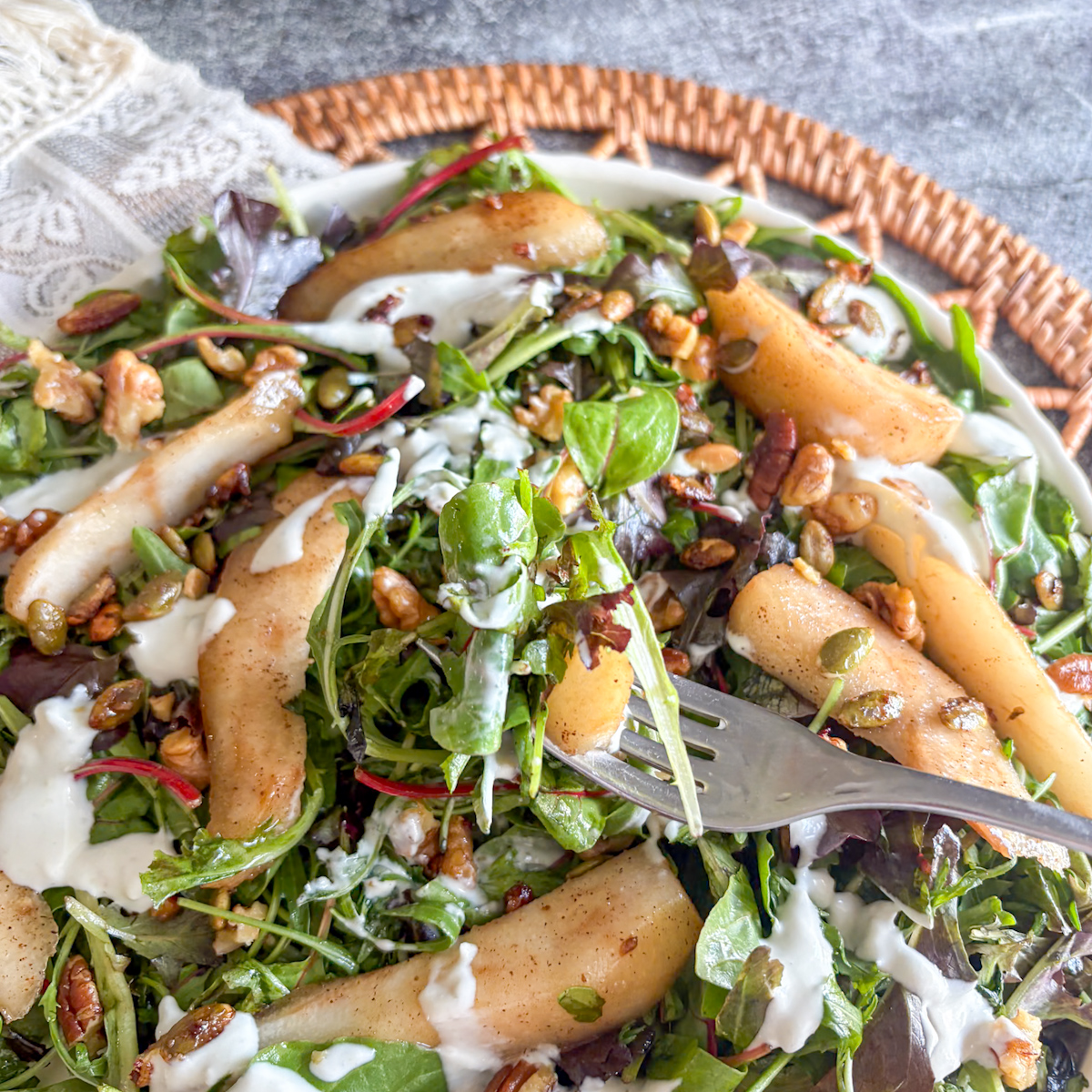 Poached pear salad with blue cheese dressing, candied nuts and salad leaves, fork lifting a bite