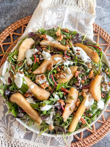 Poached pear salad with blue cheese dressing drizzled over pears, nuts and mixed leaves on a plate