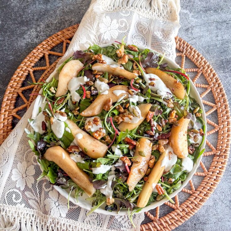 Poached pear salad with blue cheese dressing drizzled over pears, nuts and mixed leaves on a plate