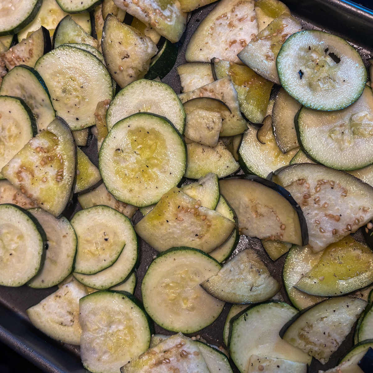 Sliced courgette and aubergine on a metal tray ready for roasting for an aubergine salad