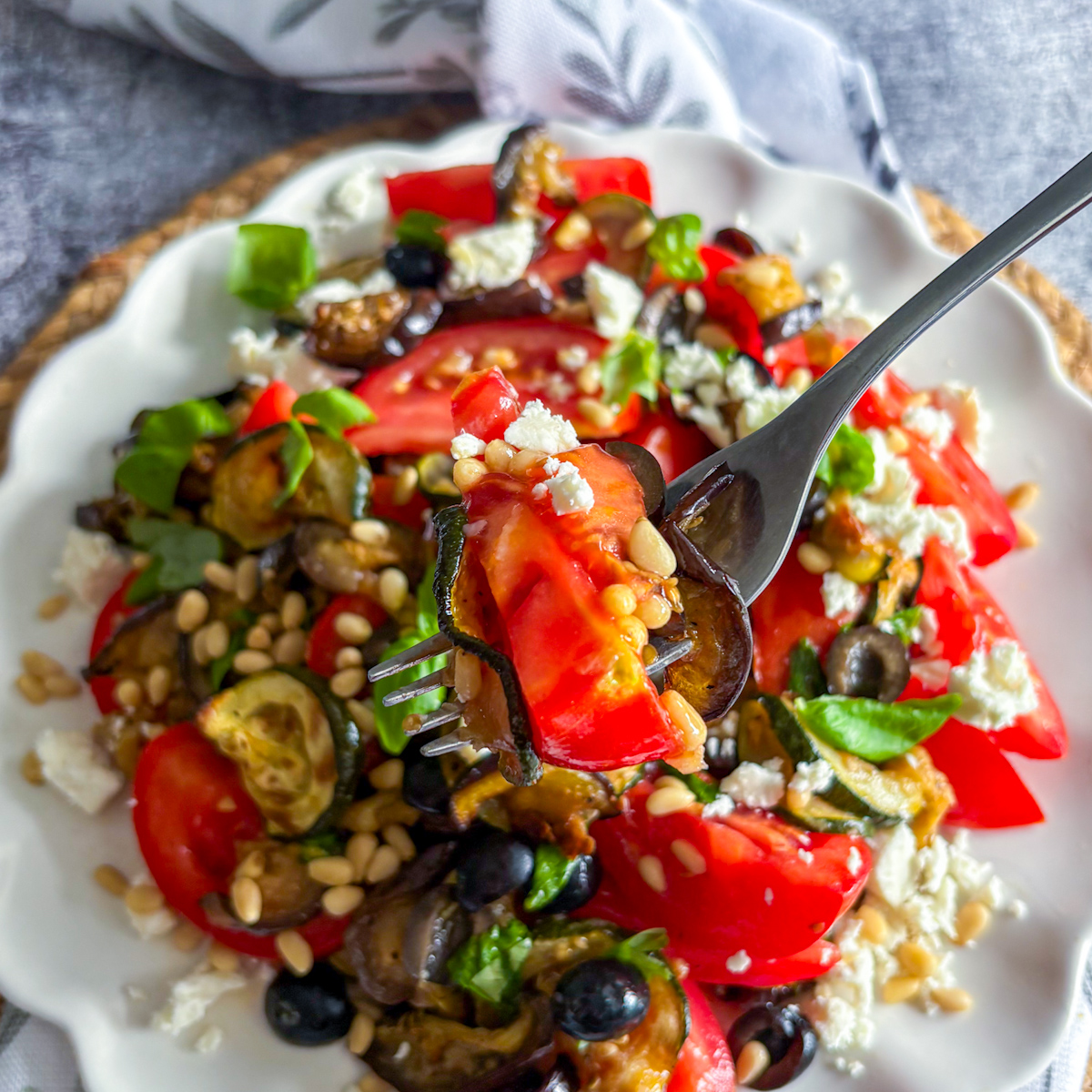 Forkful of roasted courgette and aubergine salad with tomato, olives and feta
