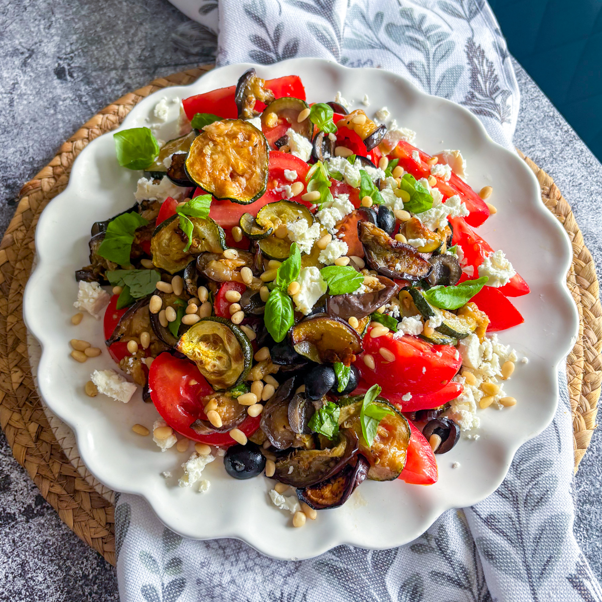  Roasted courgette and aubergine salad with tomatoes, black olives, feta and pine nuts on a white plate
