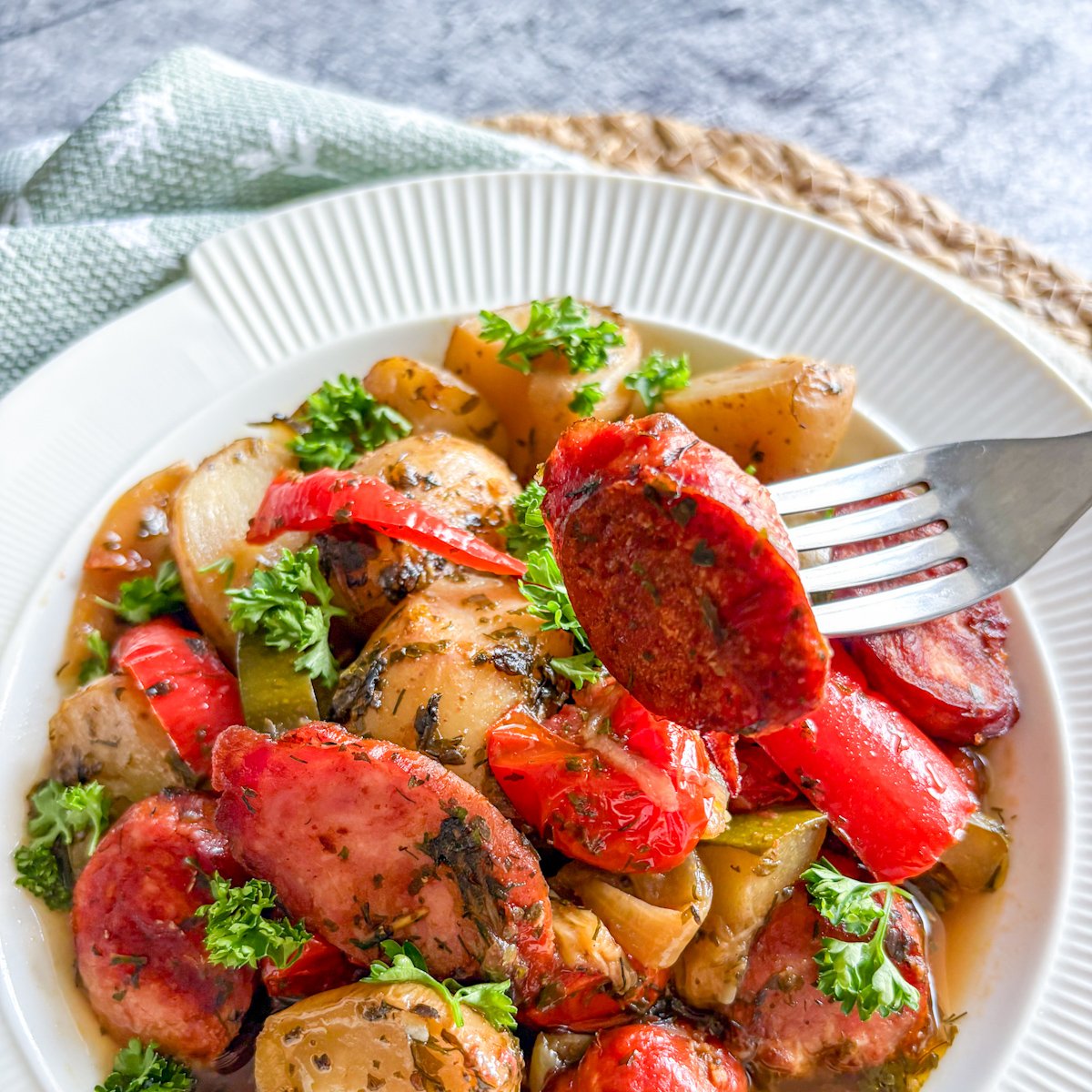 Forkful of crispy kielbasa above an easy sausage and potato stew with peppers and tomatoes