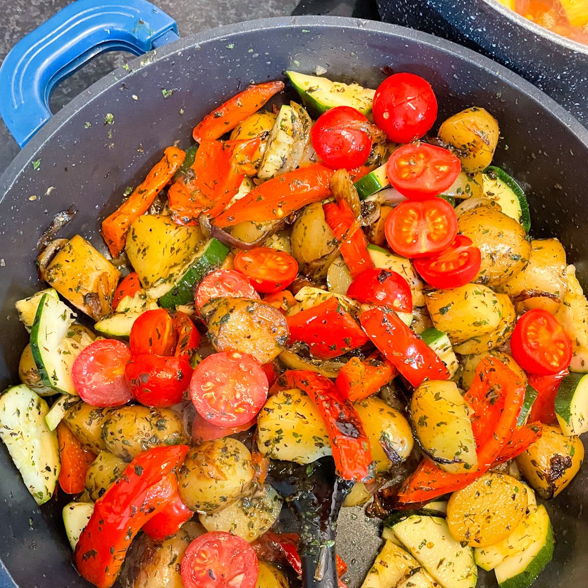Smoked sausage stew in a pan with halved cherry tomatoes, courgette, baby potatoes and peppers