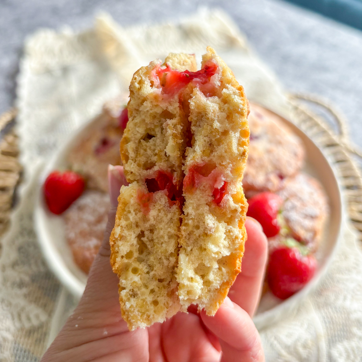 Hand holding a strawberry oatmeal cookie broken in half, showing soft crumb and juicy fresh strawberry pieces