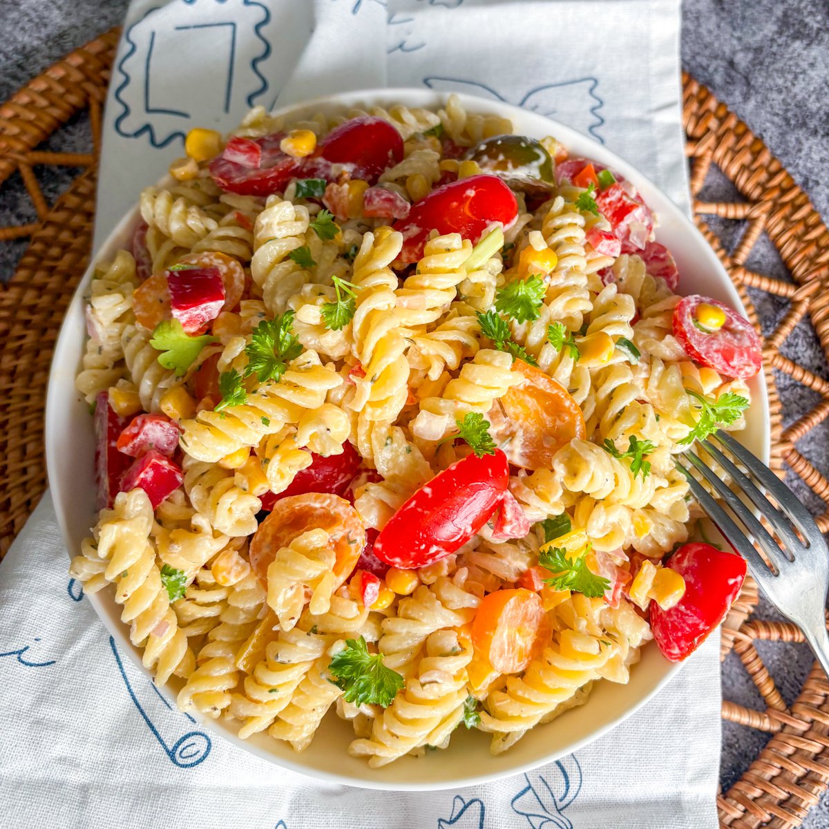 Bowl of summer pasta salad with creamy dressing, bell peppers and sweetcorn on a linen napkin