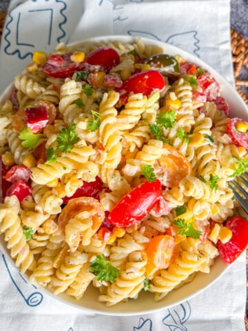 Creamy summer pasta salad with cherry tomatoes, peppers and corn in a white bowl, fork resting