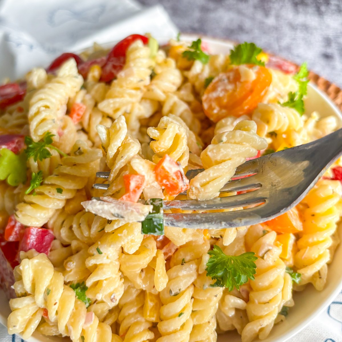 Fork lifting creamy summer pasta salad from a bowl filled with tomatoes and sweetcorn
