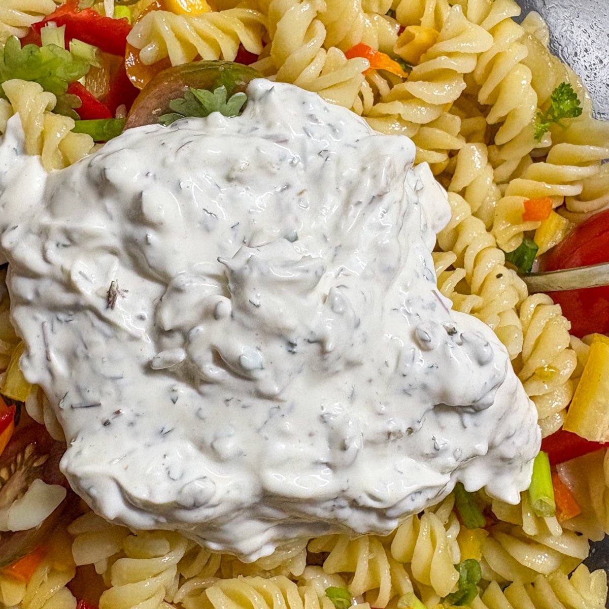Creamy mayo-yogurt dressing being spooned over summer pasta salad ingredients before mixing