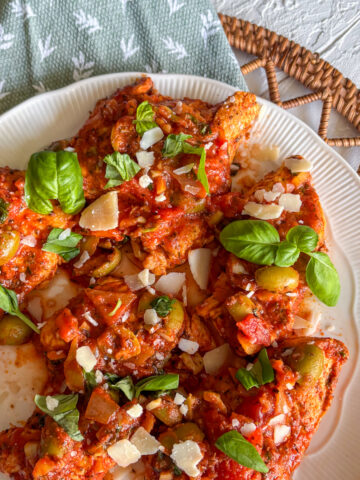 Italian turkey steaks in tomato sauce garnished with basil and parmesan on a white plate