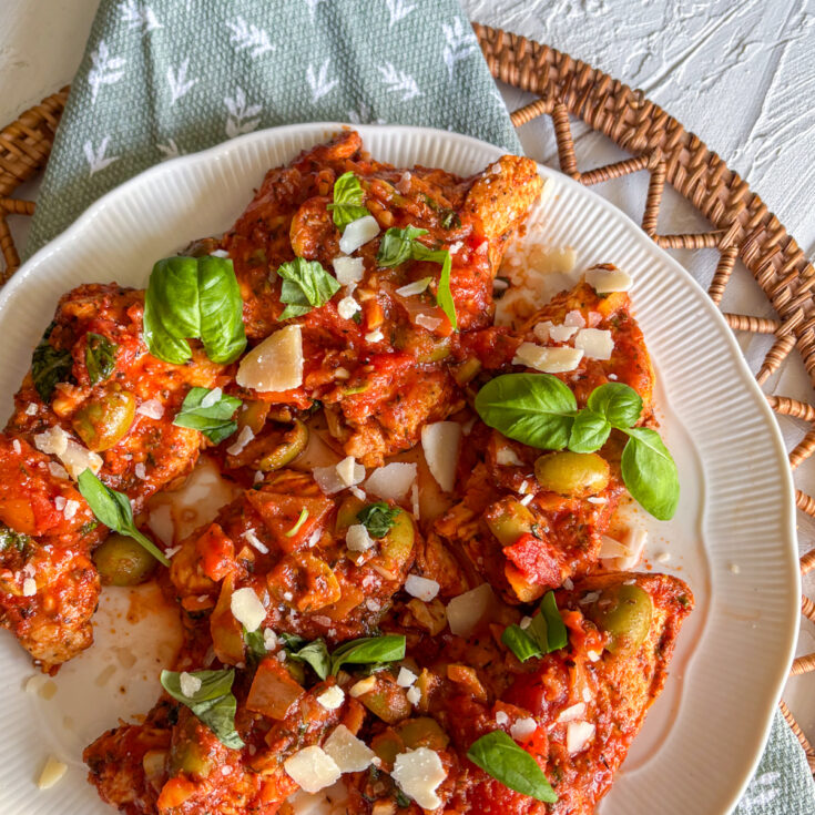 Italian turkey steaks in tomato sauce garnished with basil and parmesan on a white plate
