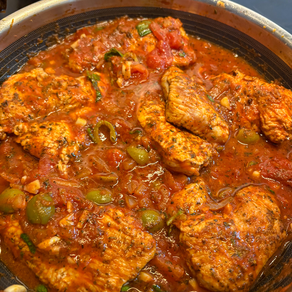 Turkey steaks simmering in tomato sauce with green olives in a large skillet