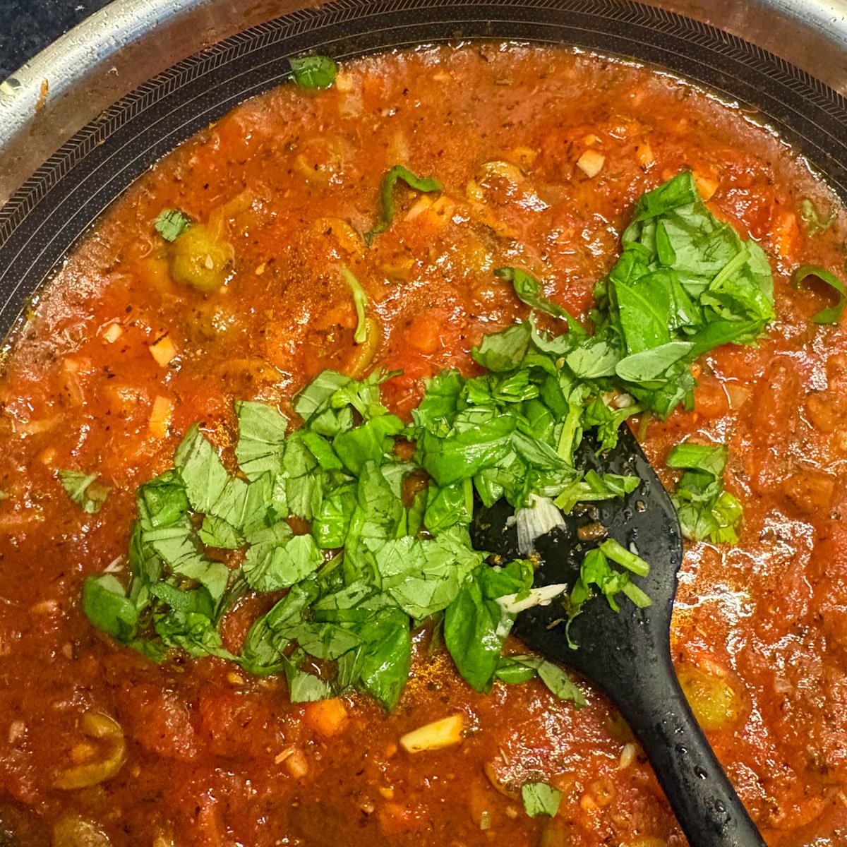 Tomato sauce with torn fresh basil being stirred in a pan for turkey steaks