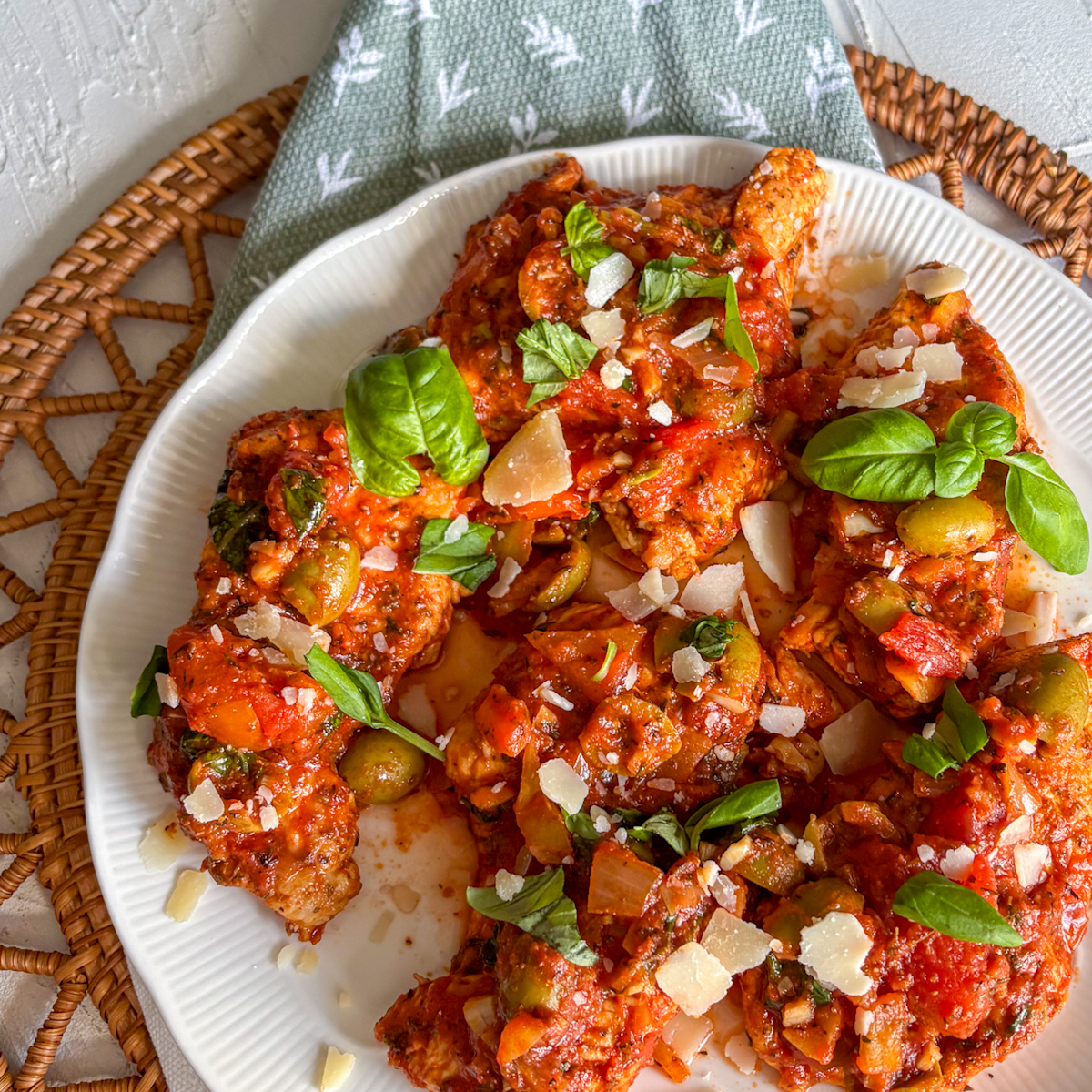 Plate of turkey in tomato sauce with green olives, fresh basil and parmesan on a woven mat