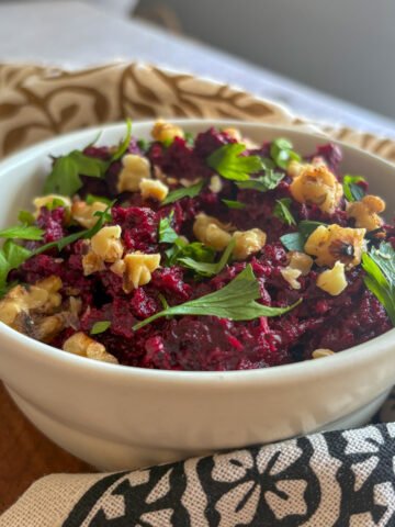 Beetroot and walnut dip in a sunlit white bowl on a wooden board, topped with crunchy walnuts and parsley