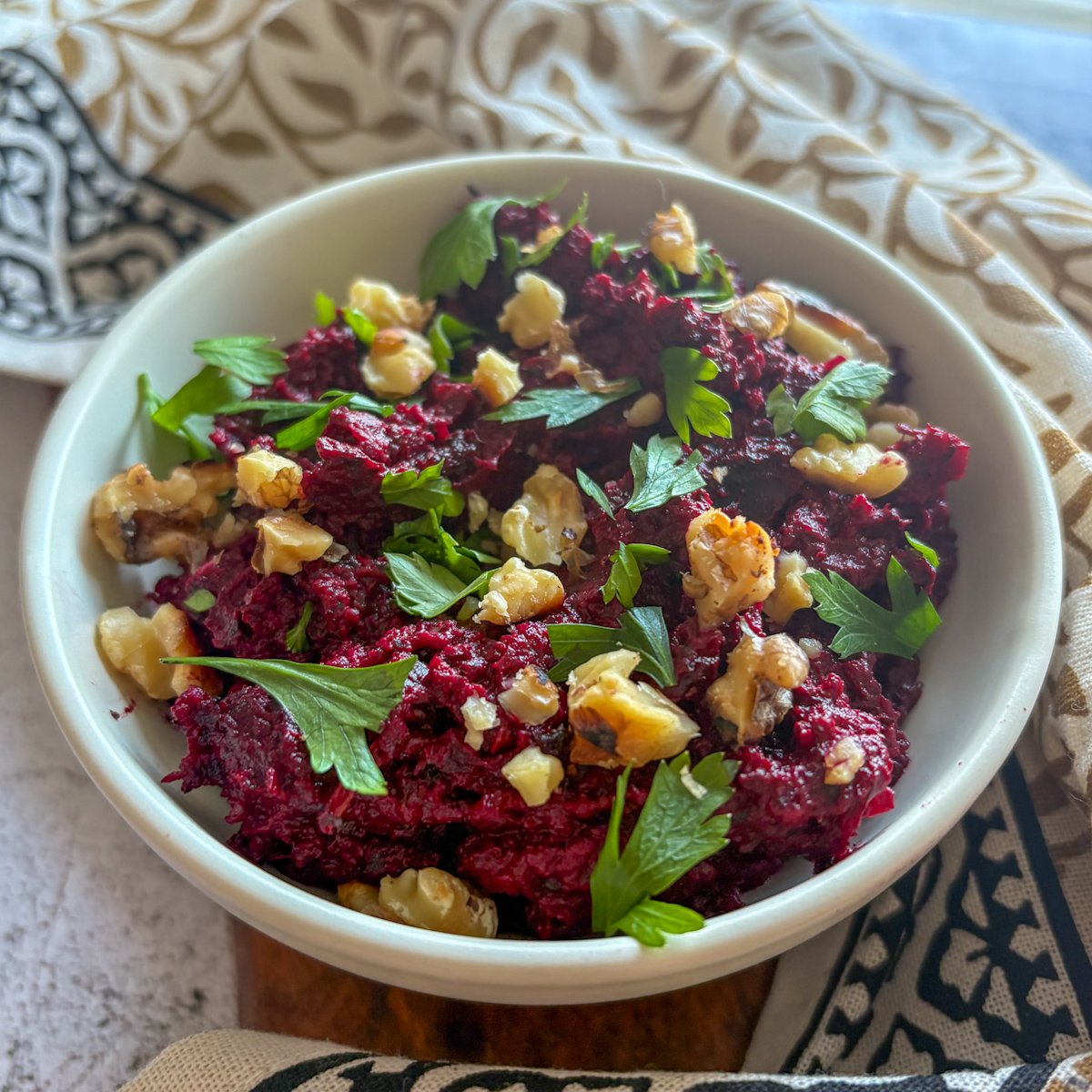 Beetroot and walnut dip with ruby-red texture, toasted walnuts and fresh parsley, styled with patterned linens