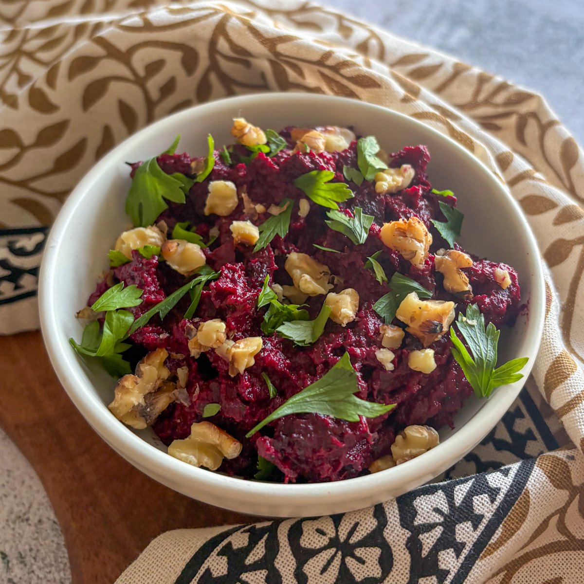 Beetroot and walnut dip in a deep white bowl on a wooden board by a bright window, topped with parsley