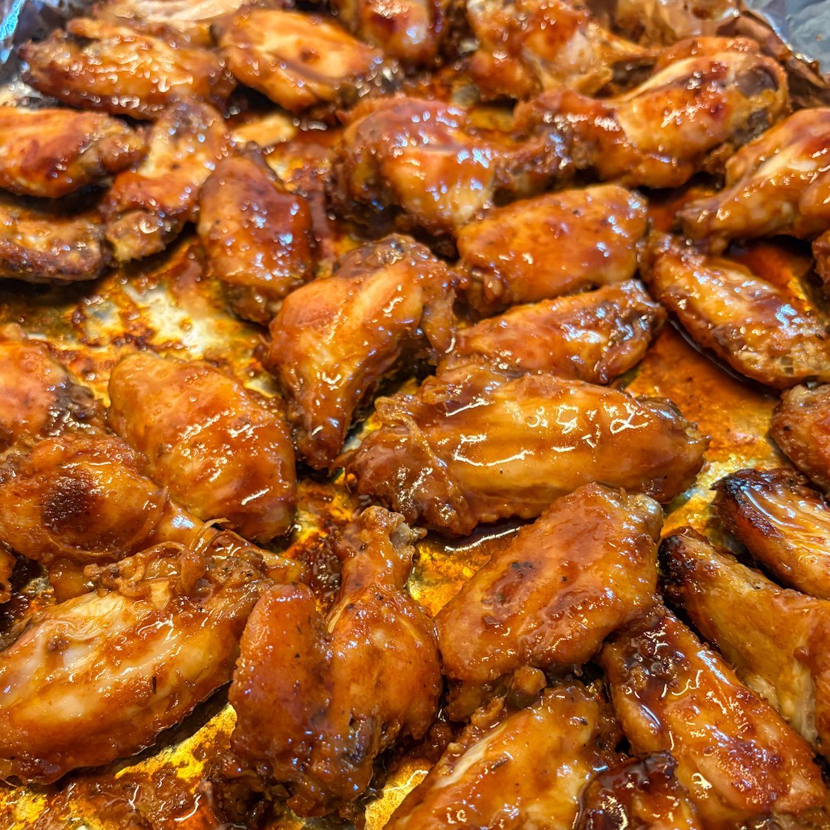 Freshly baked Guinness chicken wings on a foil-lined tray straight from the oven, glossy with sticky glaze before plating.