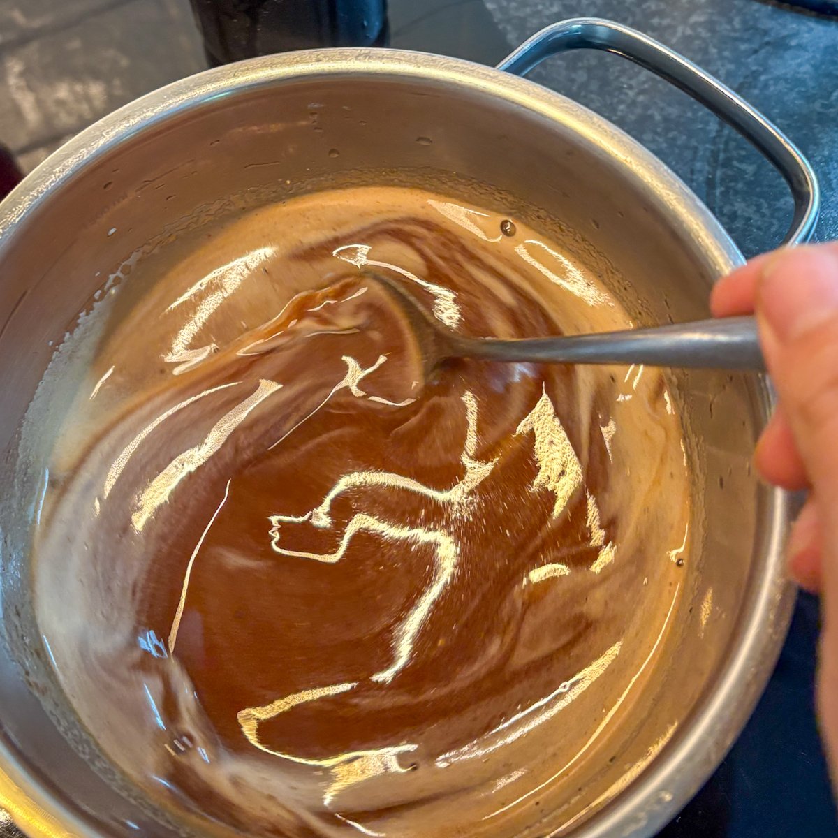 Guinness glaze reducing in a stainless steel saucepan, glossy and dark, with a spoon drawing a line through the thickened sauce.