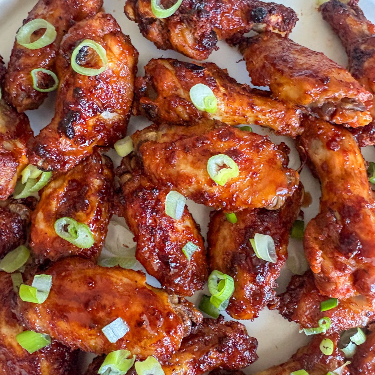 Close-up of Guinness chicken wings with caramelised, sticky skin and spring onions, stacked on a plate