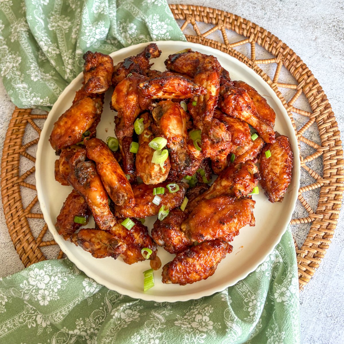 Overhead close-up of sticky Guinness chicken wings on a cream plate over a rattan mat, garnished with spring onions.