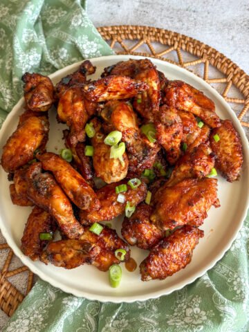 Baked Guinness chicken wings piled on a plate with a green floral napkin and woven mat, glazed and topped with spring onions.